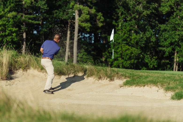 man hitting golf ball out of sand trap