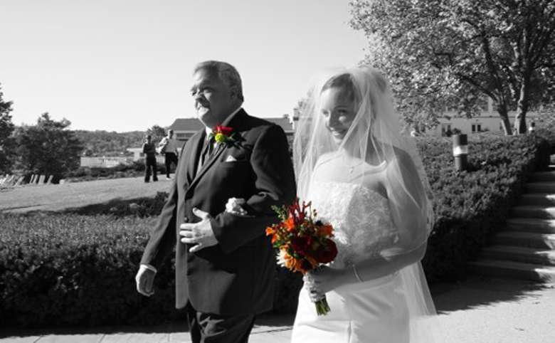 Woman and father walking down the aisle in black and white with bright orange and red bouquets