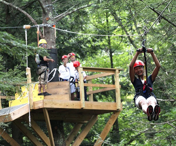 woman on a zipline while family members watch from a platform