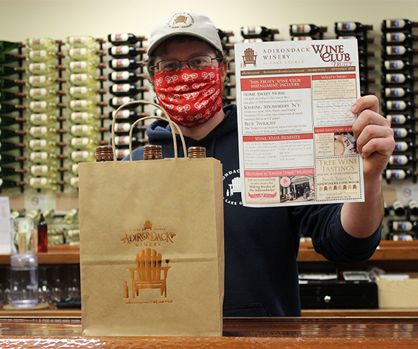 man wearing face mask holding a wine club membership application and standing in front of Adirondack Winery wine