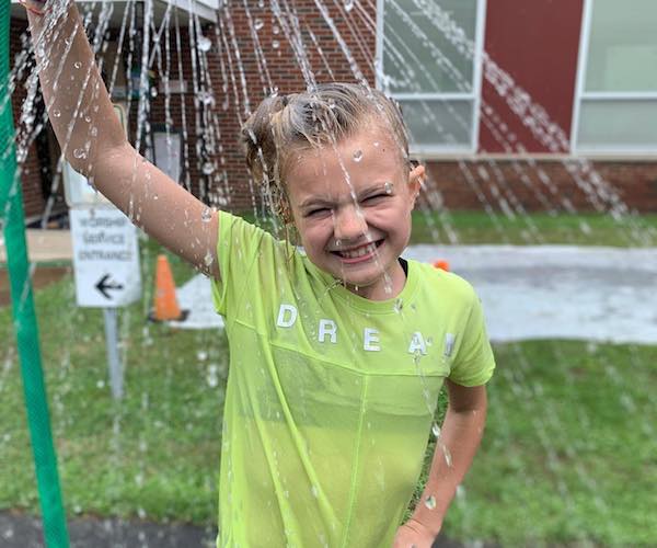 girl playing under a sprinkler and smiling