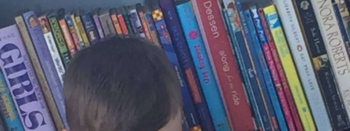 little boy in front of bookshelf holding up a book