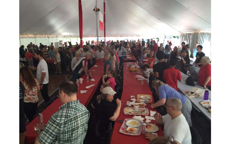 lines of tables under a big tent with people eating at them