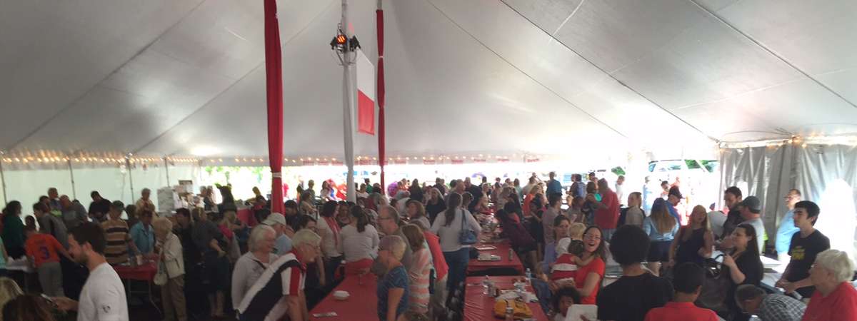 lines of tables under a big tent with people eating at them