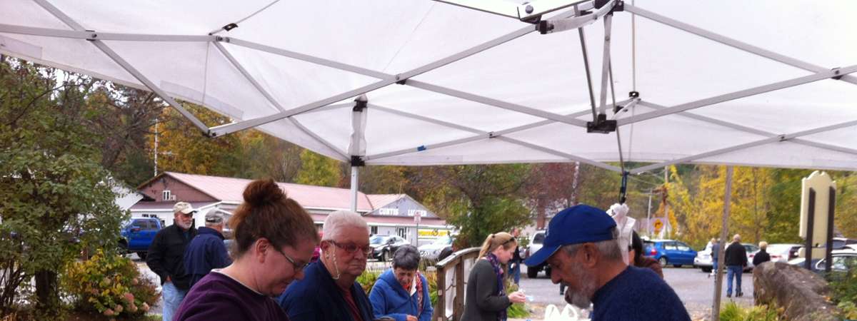 shoppers under a white tent checking out veggies