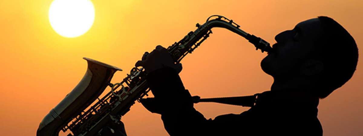 Man playing a saxaphone in front of a sunset