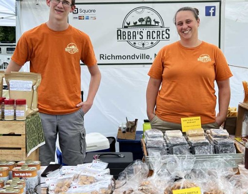 abba's acres stand with variety of goods on table and two people smiling for photo