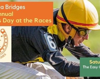 A jockey wearing a yellow hat riding a horse in a race with the Saratoga Bridges logo surrounded by a horseshoe.