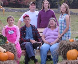 family poses by pumpkins and hay bales