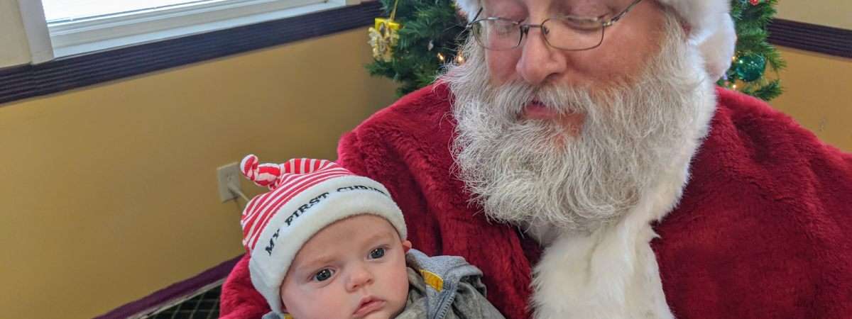 santa looks down at baby with my first christmas hat on