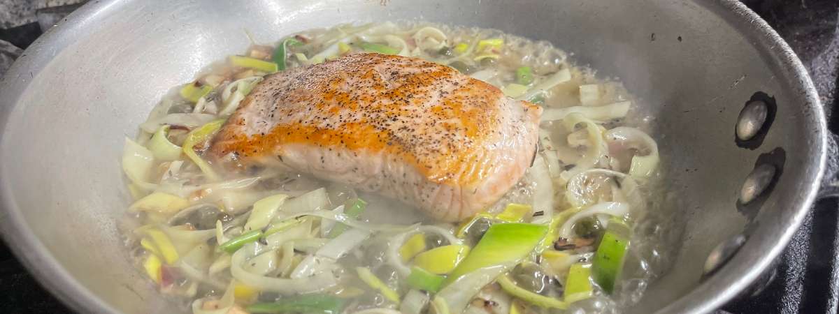fish cooking in a pan with veggies
