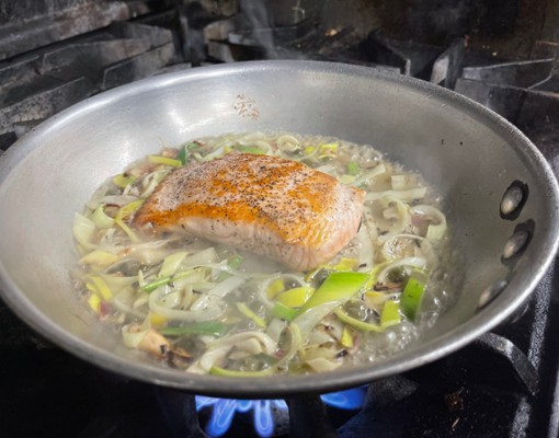 fish cooking in a pan with veggies