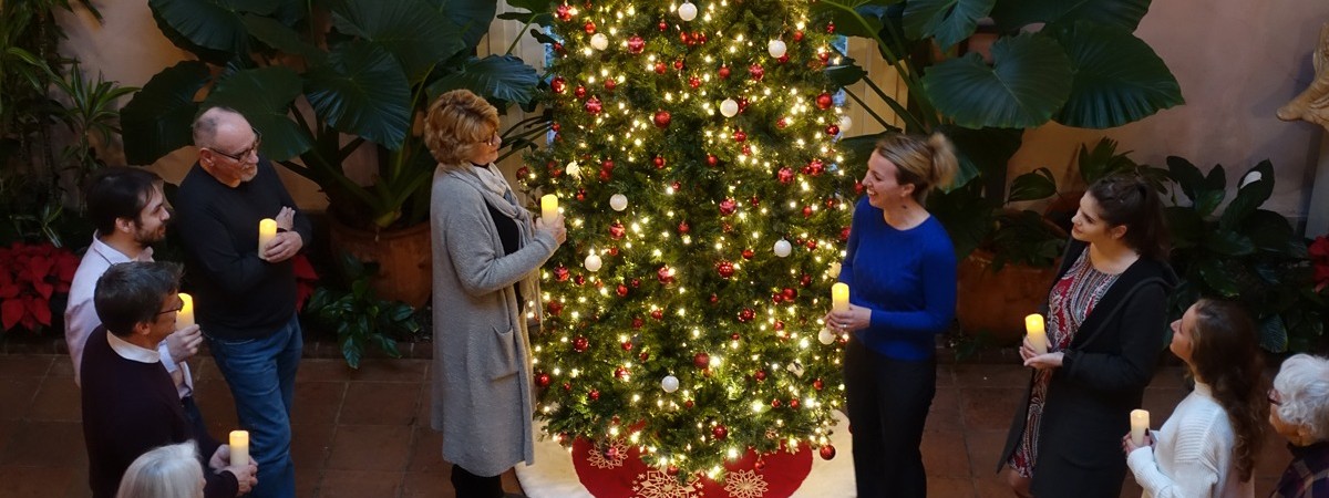 people with candles gathered around a christmas tree