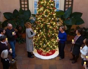 people with candles gathered around a christmas tree