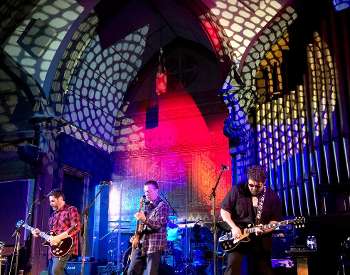 three men with guitars perform on stage