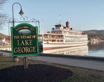 cruise ship behind welcome to the village of lake george sign