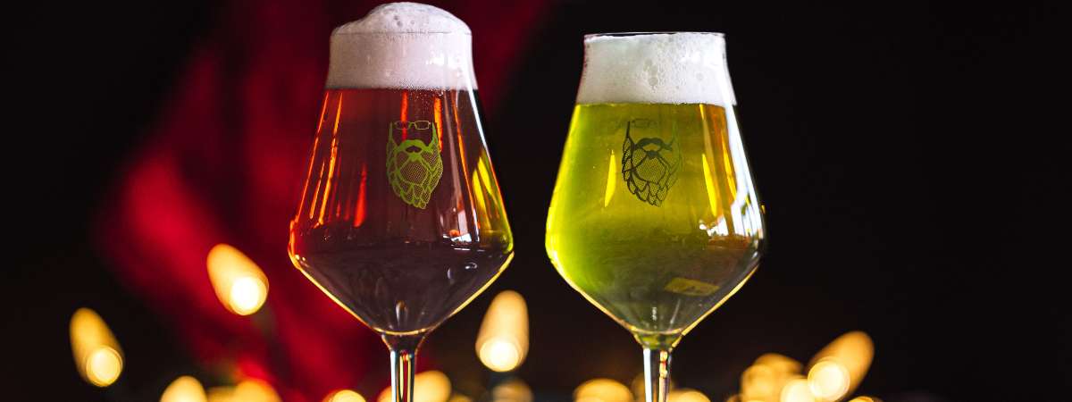 Two beer glasses, one red and one green in front of Christmas lights.