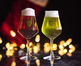 Two beer glasses, one red and one green in front of Christmas lights.