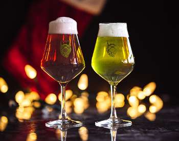 Two beer glasses, one red and one green in front of Christmas lights.
