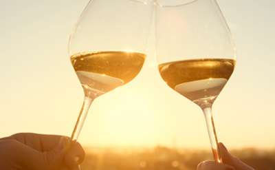 Two glasses of wine cheers-ing over a sunset sky