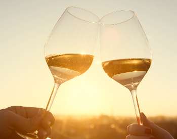 Two glasses of wine cheers-ing over a sunset sky