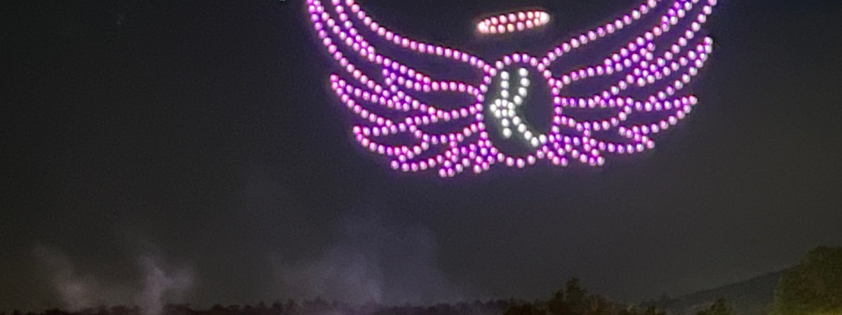Purple and blue colored drones in the sky shaped as the Kelly's Angels logo