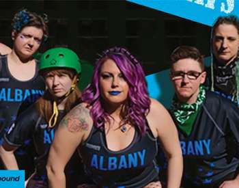Roller derby skaters pose in front of building