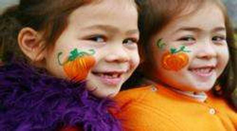 two little girls with pumpkins painted on their cheesk