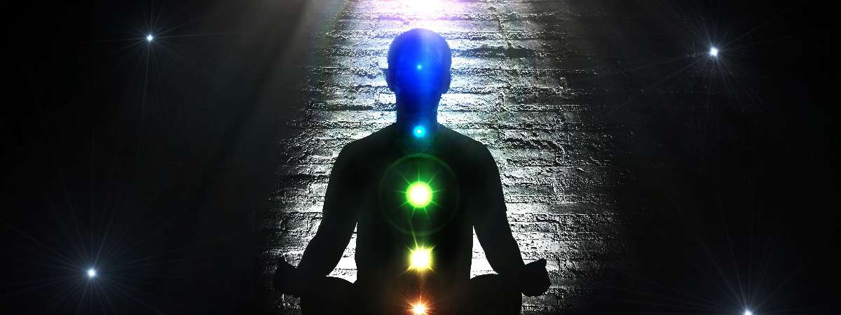 Shadow of a person meditating with chakras lit