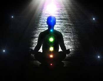 Shadow of a person meditating with chakras lit