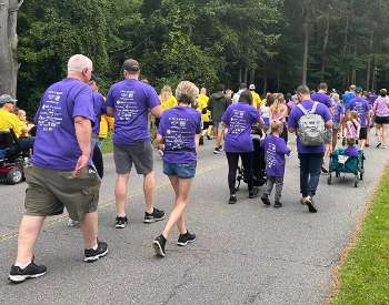 Group of individuals walking away from the camera. Majority of individuals are wearing purple tshirts