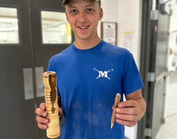 student holds finished candlestick and pen