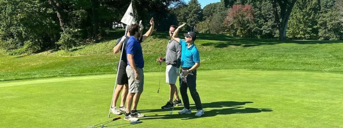 Golfers celebrating with a high five near the hole on a golf course.