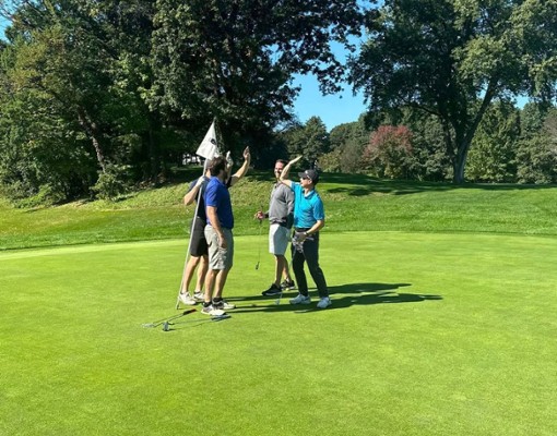 Golfers celebrating with a high five near the hole on a golf course.