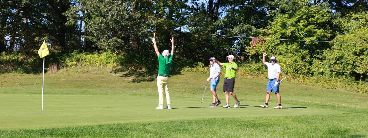 Golfers celebrating with their arms in the air  near the hole on a golf course.