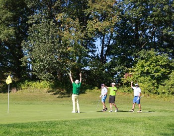 Golfers celebrating with their arms in the air  near the hole on a golf course.
