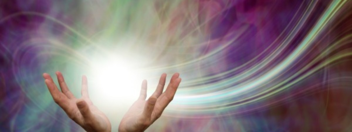 Hands in an open and up position holding energy and light. Rays of light streaming from the hands with an array of colors in the background.