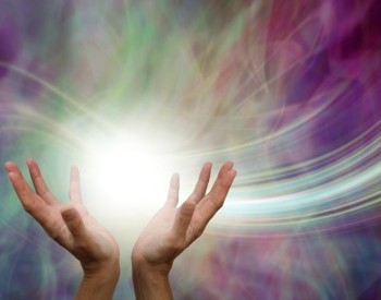 Hands in an open and up position holding energy and light. Rays of light streaming from the hands with an array of colors in the background.