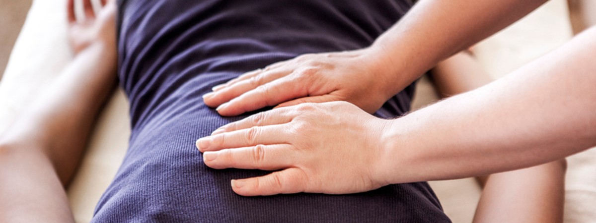 Person laying face down on a table with a practitioner placing their hands on the client's back.