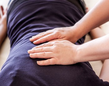 Person laying face down on a table with a practitioner placing their hands on the client's back.