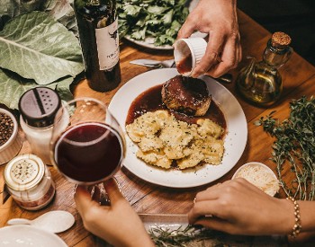 Plate of food, sides like pepper, a glass of red wine in hand