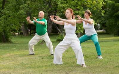 Three people outside moving in qigong
