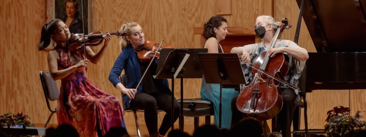 A violinist, violist, cellist, and grand piano player perform a concert