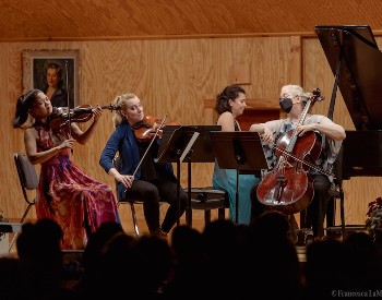 A violinist, violist, cellist, and grand piano player perform a concert