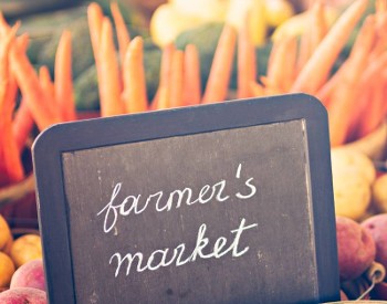 farmers market sign in front of carrots and potatoes