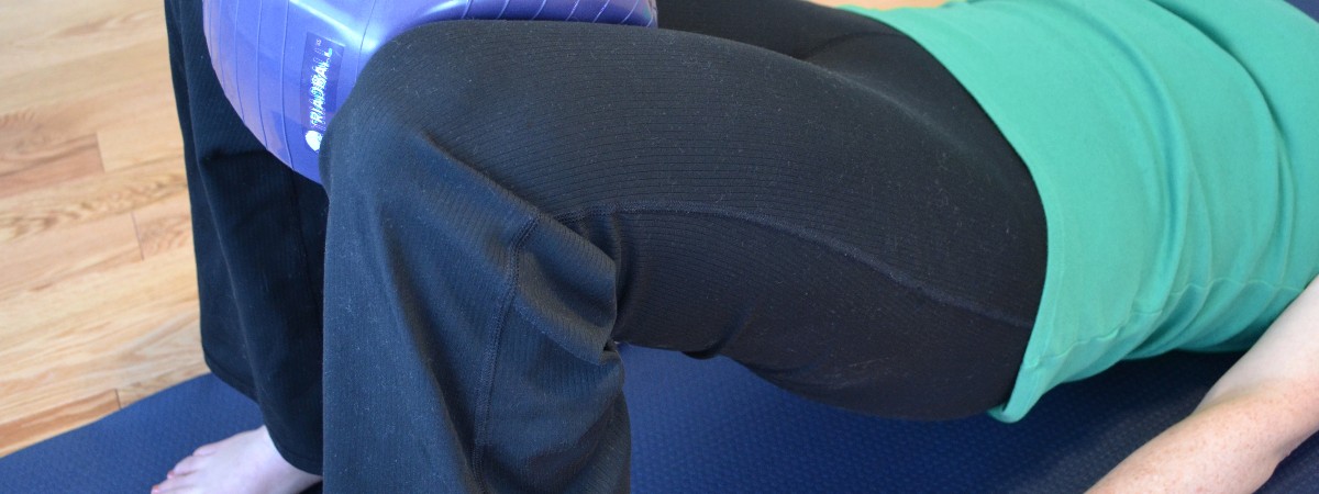 A woman wearing a green shirt, black pants with a triadball between her knees