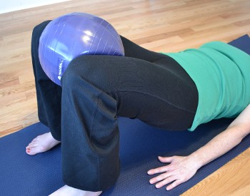 A woman wearing a green shirt, black pants with a triadball between her knees