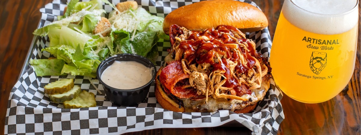 Wagyu Whole Hog burger with pulled pork, ham, bacon, cheddar cheese and BBQ sauce served with draft beer at Nature&rsquo;s Edge Bistro restaurant in Saratoga Springs