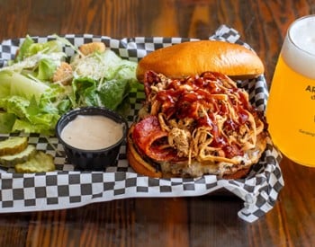 Wagyu Whole Hog burger with pulled pork, ham, bacon, cheddar cheese and BBQ sauce served with draft beer at Nature&rsquo;s Edge Bistro restaurant in Saratoga Springs
