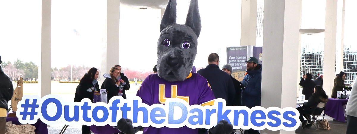 Damien the University at Albany mascot holding a "out of the darkness" sign.